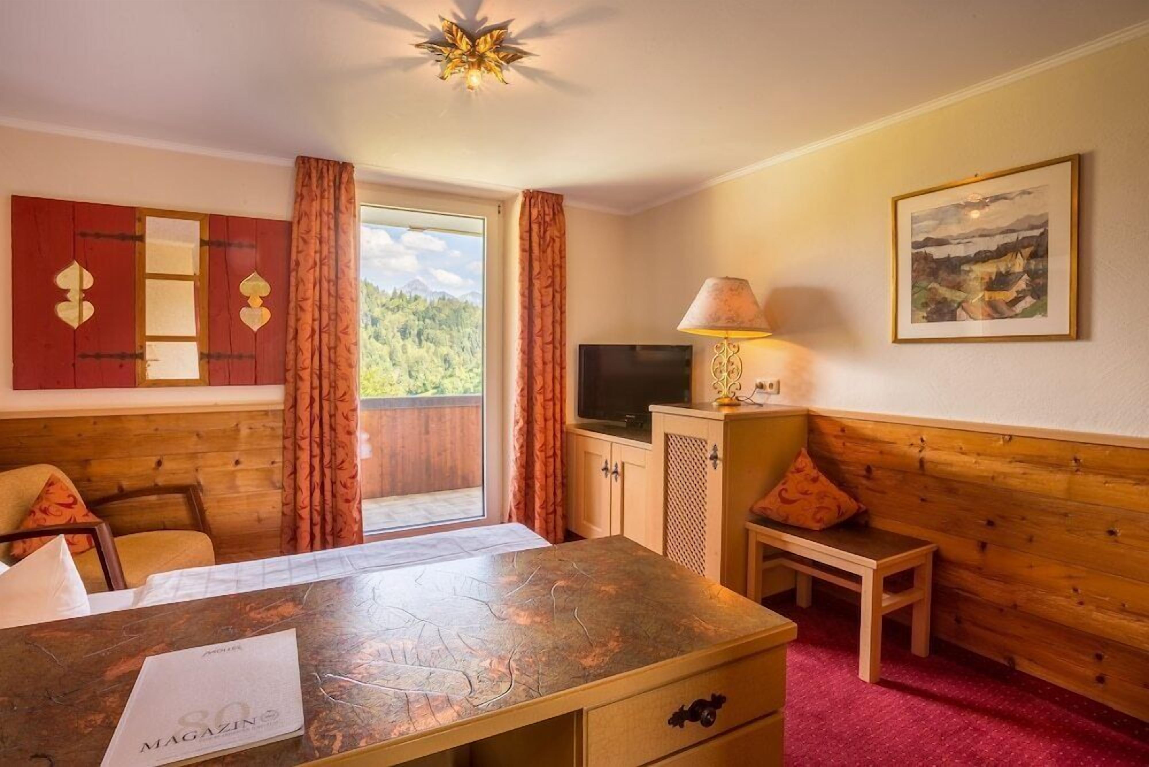 A room with a wooden headboard, a desk with a magazine, a television, and a window with curtains.