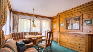 A cozy cabin interior with a striped sofa set, a wooden dining table, and a window with curtains. - Alpenhotel Oberstdorf (Oberstdorf)