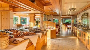 A spacious breakfast area with wooden furniture, a variety of breads and pastries, and a view of the outdoors. - Alpenhotel Oberstdorf (Oberstdorf)