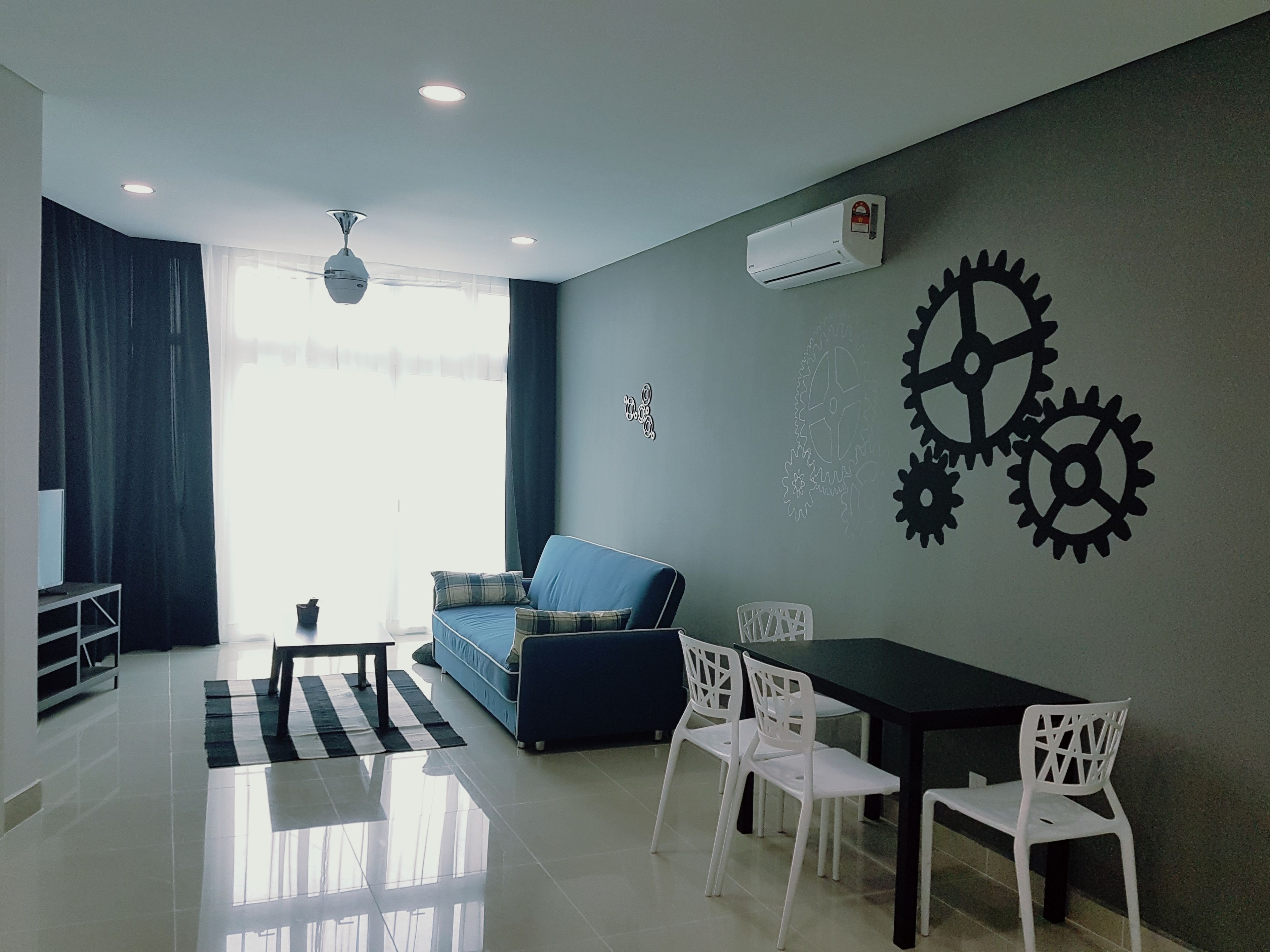 Una sala moderna con sofá, mesa de comedor y sillas. Hay un ventilador de techo, un equipo de aire acondicionado y una ventana con cortinas.