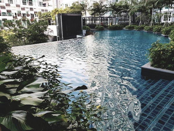 A swimming pool with clear water, surrounded by lush greenery and modern buildings in the background.