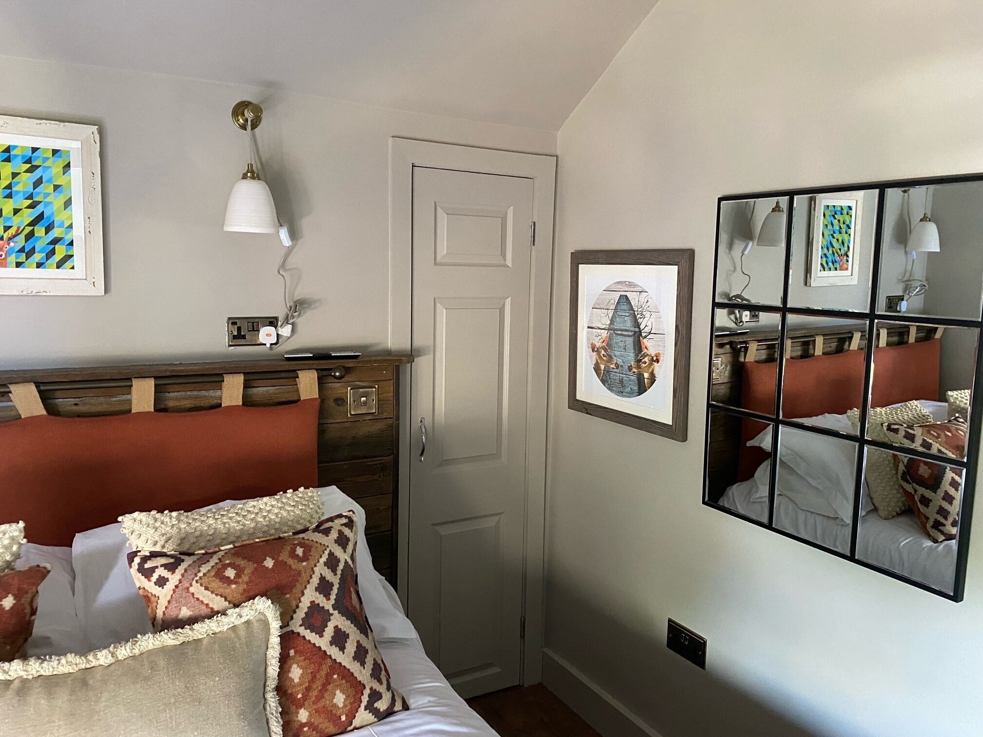 A bedroom with a bed, a dresser, a door, and a mirror with a reflection.
