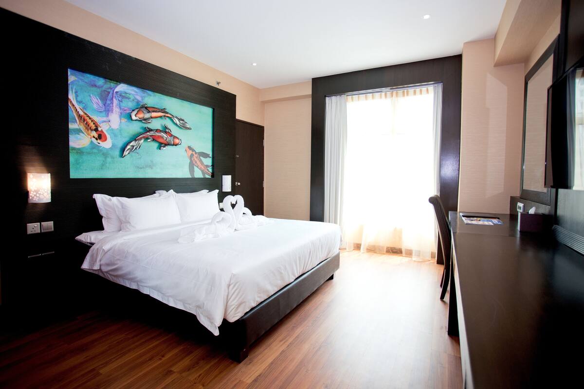A modern hotel room with a large bed, a painting of koi fish, a flat-screen TV, and a large window with curtains.
