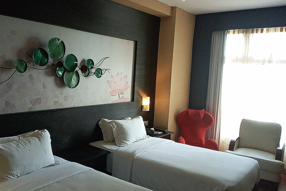 A hotel room with two beds, a large wall art piece, a red chair, and a view of the city through the window.