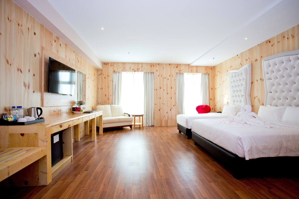 A modern hotel room with a wooden interior, a large bed, a desk with a flat-screen TV, and a seating area.