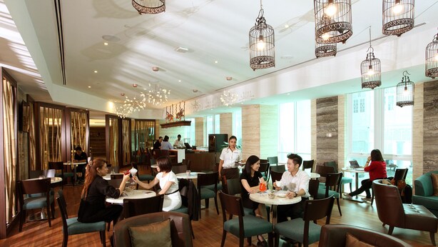 A spacious restaurant with multiple dining tables and chairs, a modern chandelier, and large windows allowing natural light. - Vouk Hotel Suites, By The Blanket (George Town)