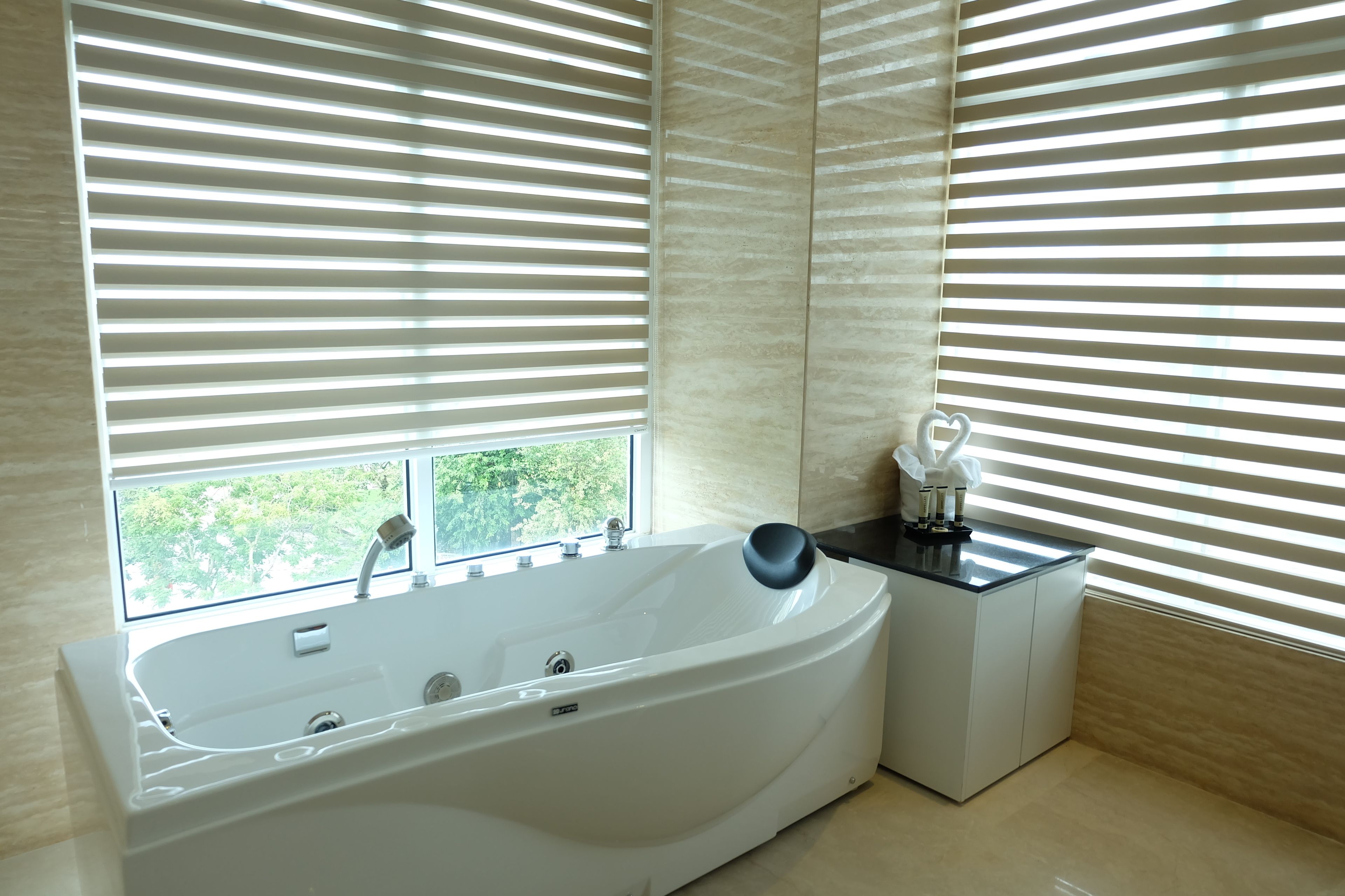 A modern bathroom with a freestanding bathtub, a small table with a vase, and a window with blinds.