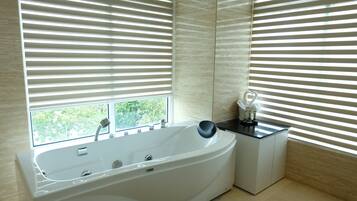 A modern bathroom with a freestanding bathtub, a small table with a vase, and a window with blinds.