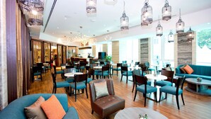 A spacious hotel lobby with multiple seating areas, including sofas and chairs, and a central dining area with tables and chairs. - Vouk Hotel Suites, By The Blanket (George Town)