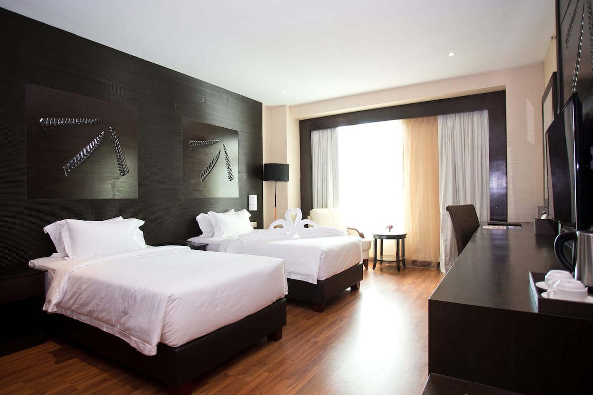 A hotel room with two beds, a desk, a TV, and a large window with curtains.