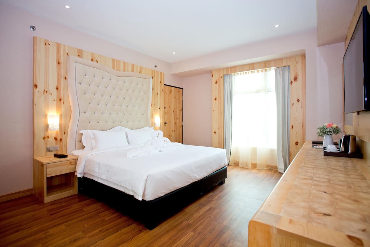 A modern hotel room with a wooden headboard, a large bed, a wooden nightstand, a flat-screen TV, and a wooden desk.