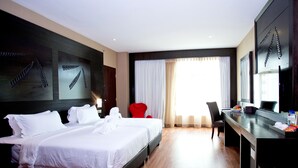 A hotel room with a large bed, a desk with a chair, a television, and a window with curtains. - Vouk Hotel Suites, By The Blanket (George Town)