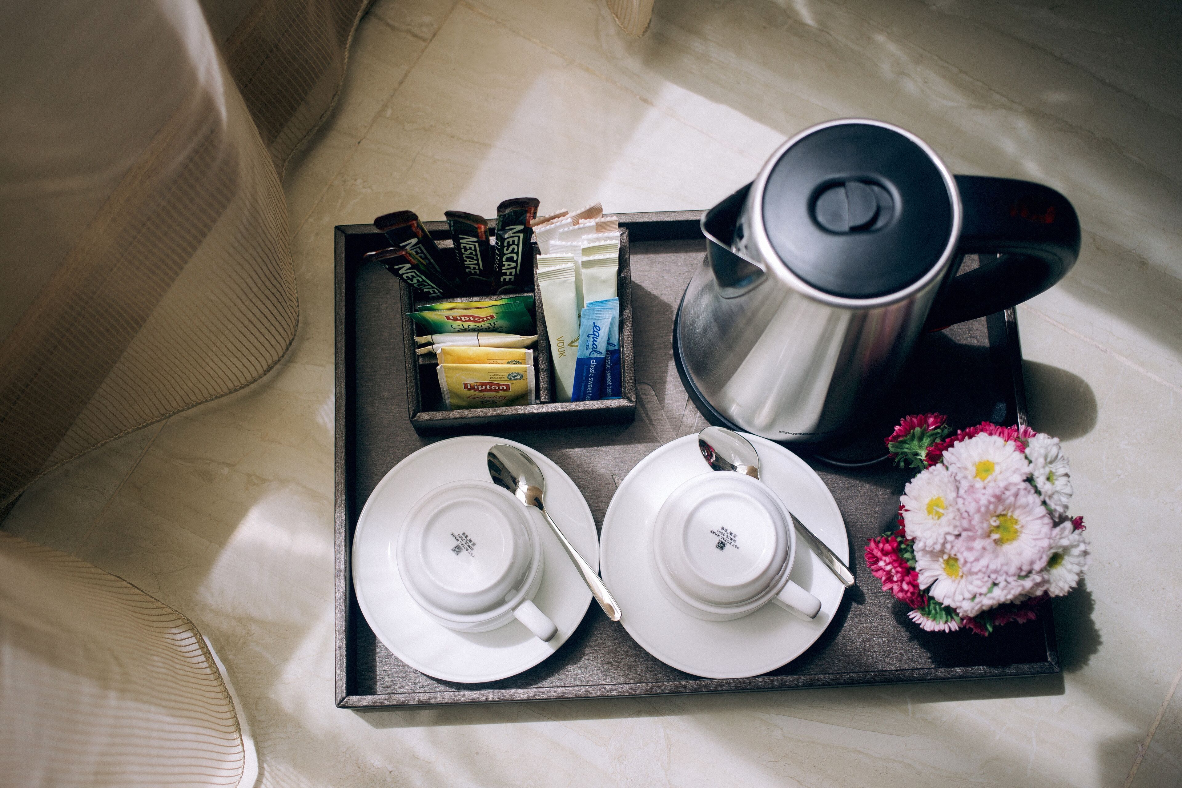 Uma bandeja com cafeteira, sachês de chá e um buquê de flores sobre a cama.