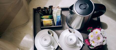 Uma bandeja com cafeteira, sachês de chá e um buquê de flores sobre a cama.