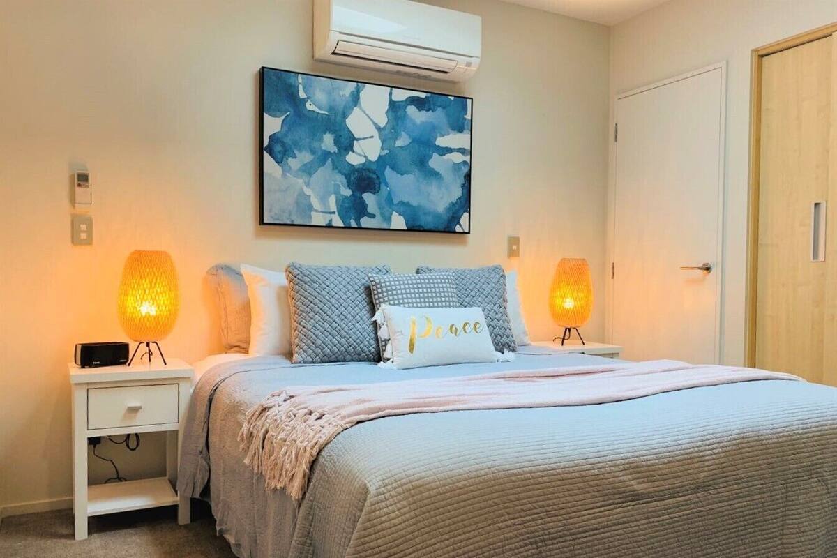 Een slaapkamer met een bed, twee bedlampen, een wandairconditioner en een schilderij.