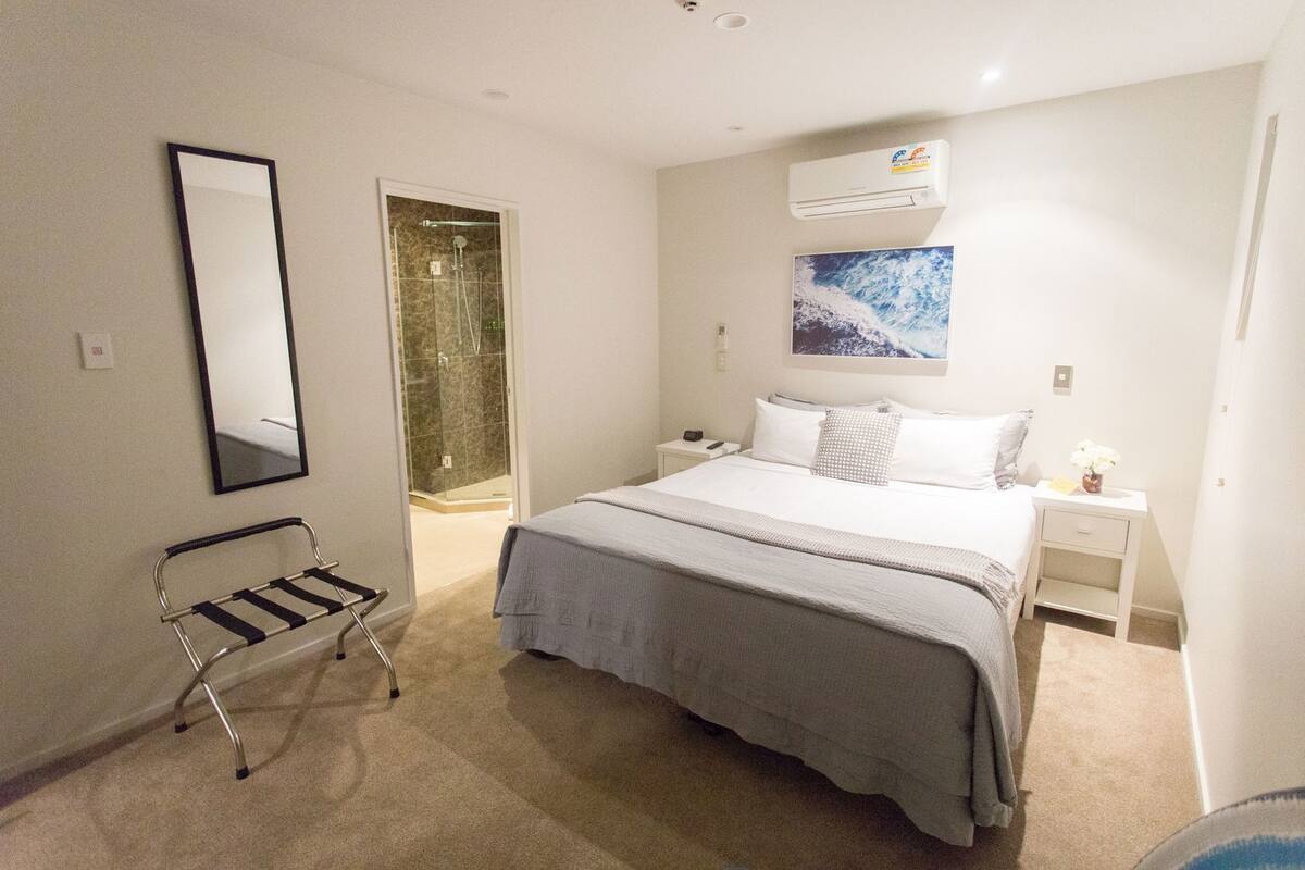Een slaapkamer met een bed, nachtkastje, spiegel, douche en een airconditioning.