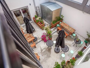A courtyard with wooden tables and chairs, potted plants, and umbrellas. - Colombo Lodge Christchurch (Christchurch)