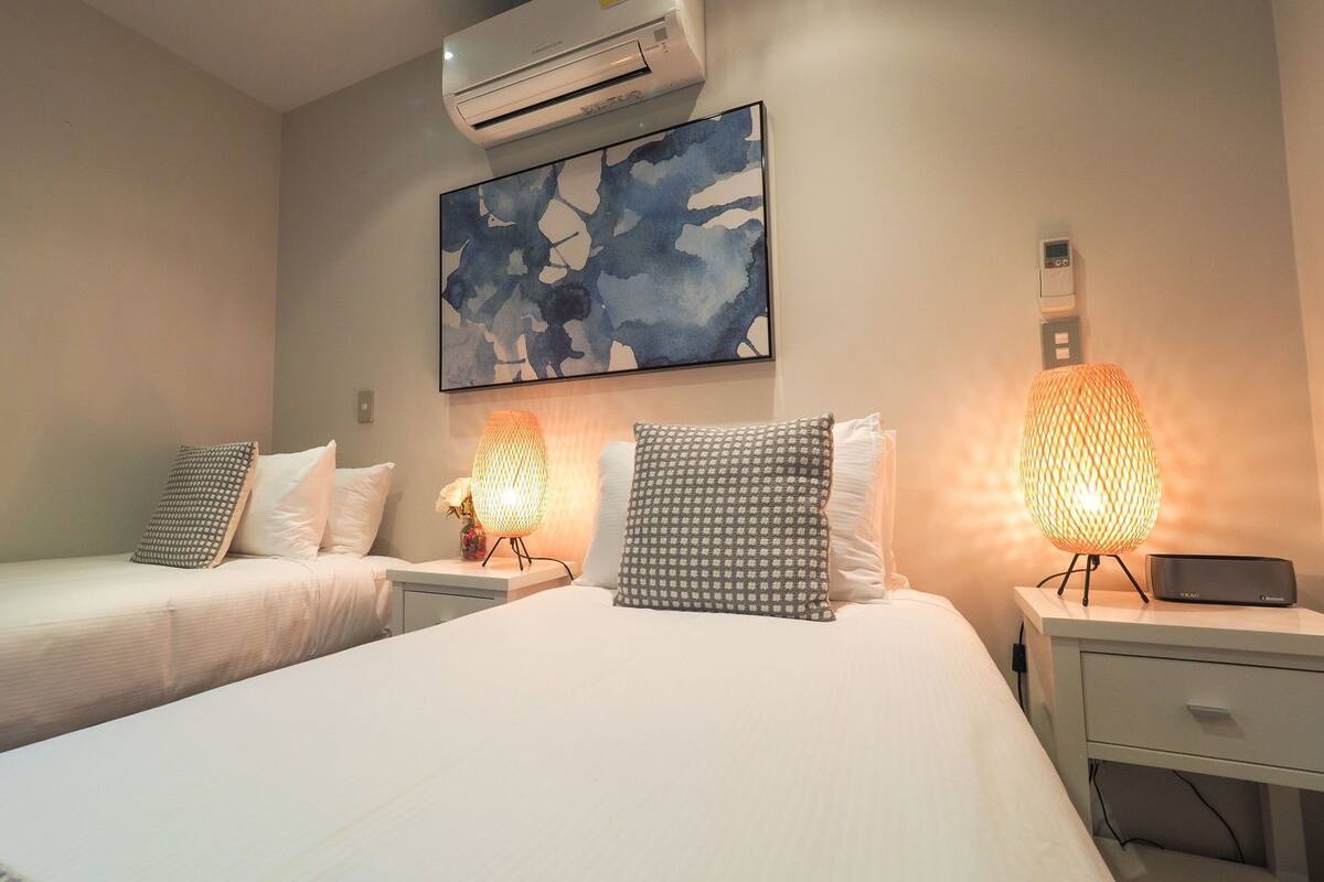 Een hotelkamer met twee bedden, een wandairconditioner, een schilderij en twee tafellampen.