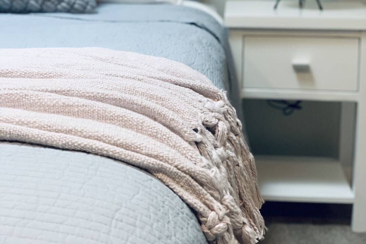 Een net opgemaakt bed met een gertextileerde deken, een bedlamp en een wanddecoratie.