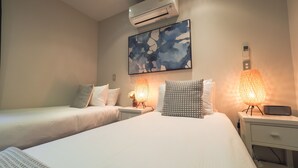 Habitación de hotel con dos camas, aire acondicionado en la pared, un cuadro y dos lámparas de mesa.