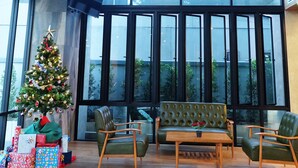 A spacious room with large windows, a modern chandelier, a Christmas tree, and green upholstered furniture. - C Cha-am Hotel (Cha-am)
