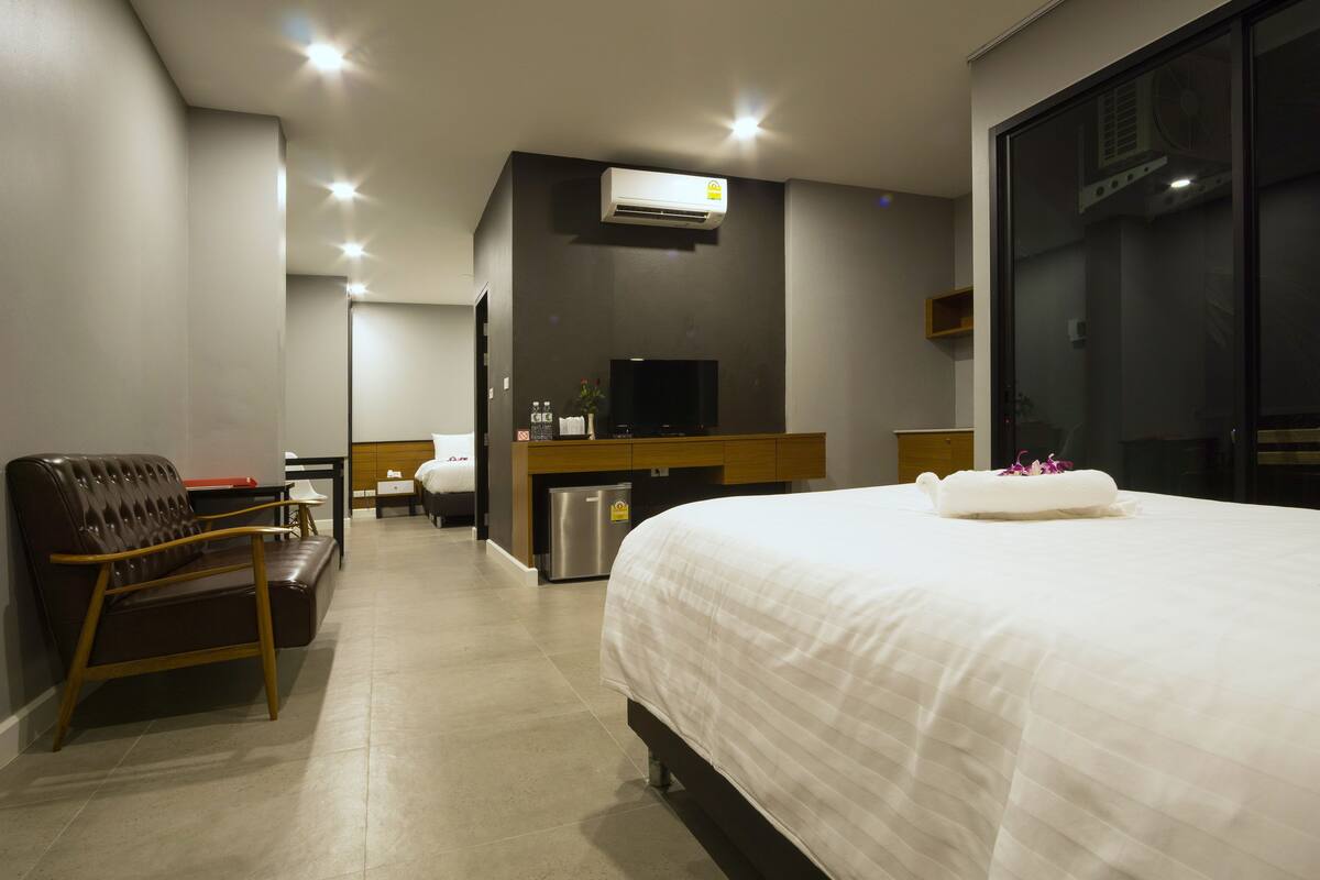 Une chambre d’hôtel avec un grand lit, un bureau avec un ordinateur, une télévision et un coin salon comprenant un canapé et un fauteuil.