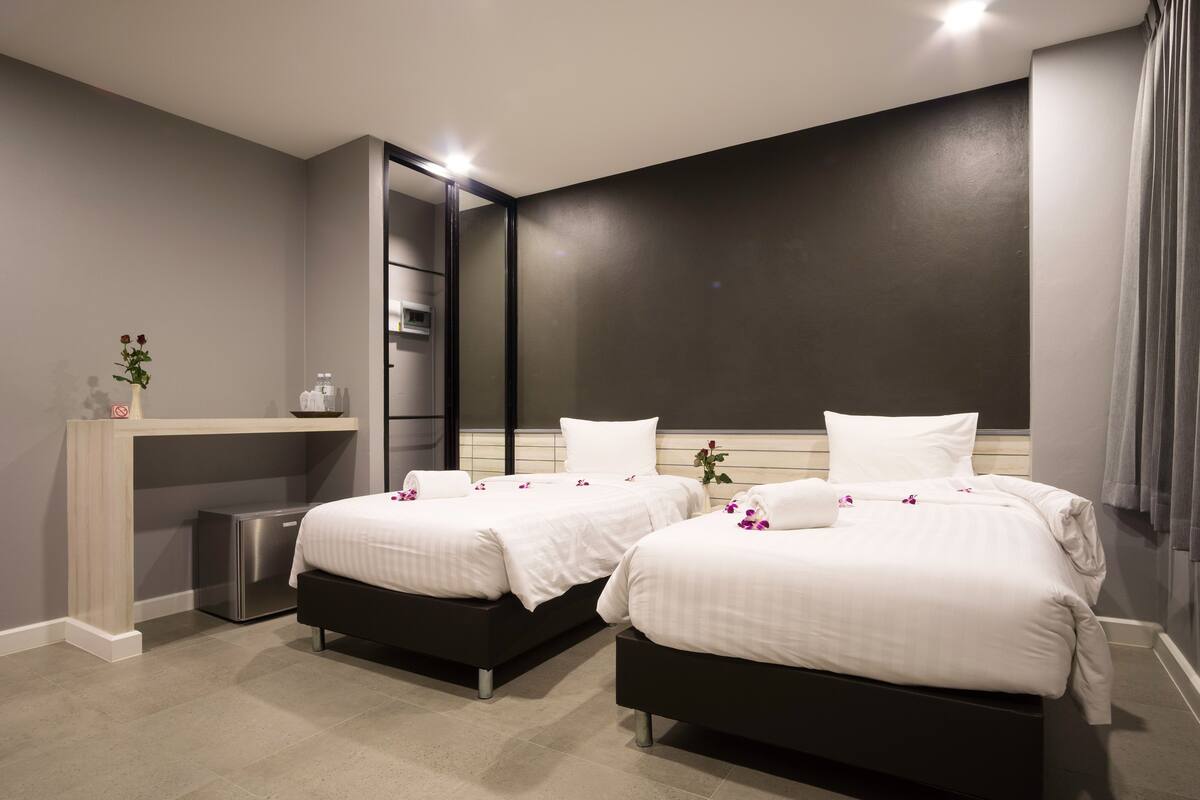 Une chambre d’hôtel moderne avec deux lits, un petit bureau et une armoire intégrée.