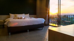 A hotel room with a large bed, a nightstand, a desk, and a balcony with a view of the sunset. - C Cha-am Hotel (Cha-am)