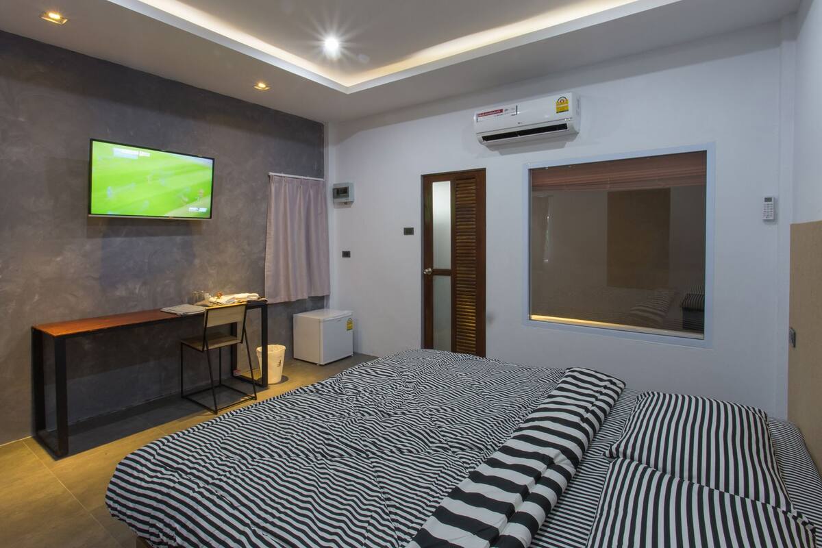 A modern bedroom with a bed, a desk, a television, and an air conditioning unit.