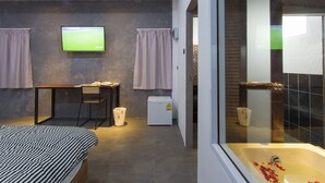 A modern bedroom with a bed, a desk, a television, and a bathroom with a bathtub. - 88 Fine Hotel (Phunphin)