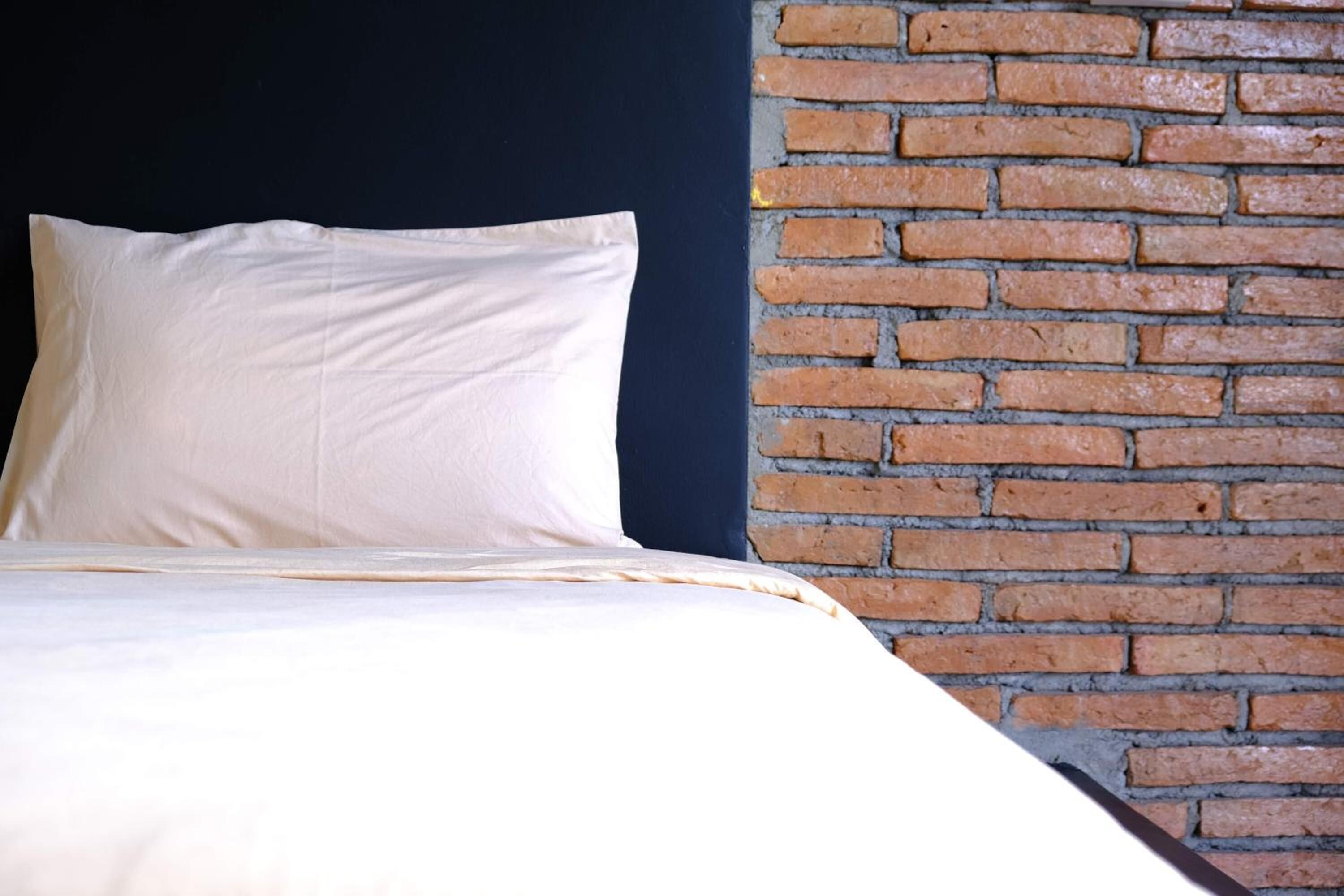 A bed with white bedding against a brick wall.