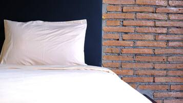 A bed with white bedding against a brick wall.
