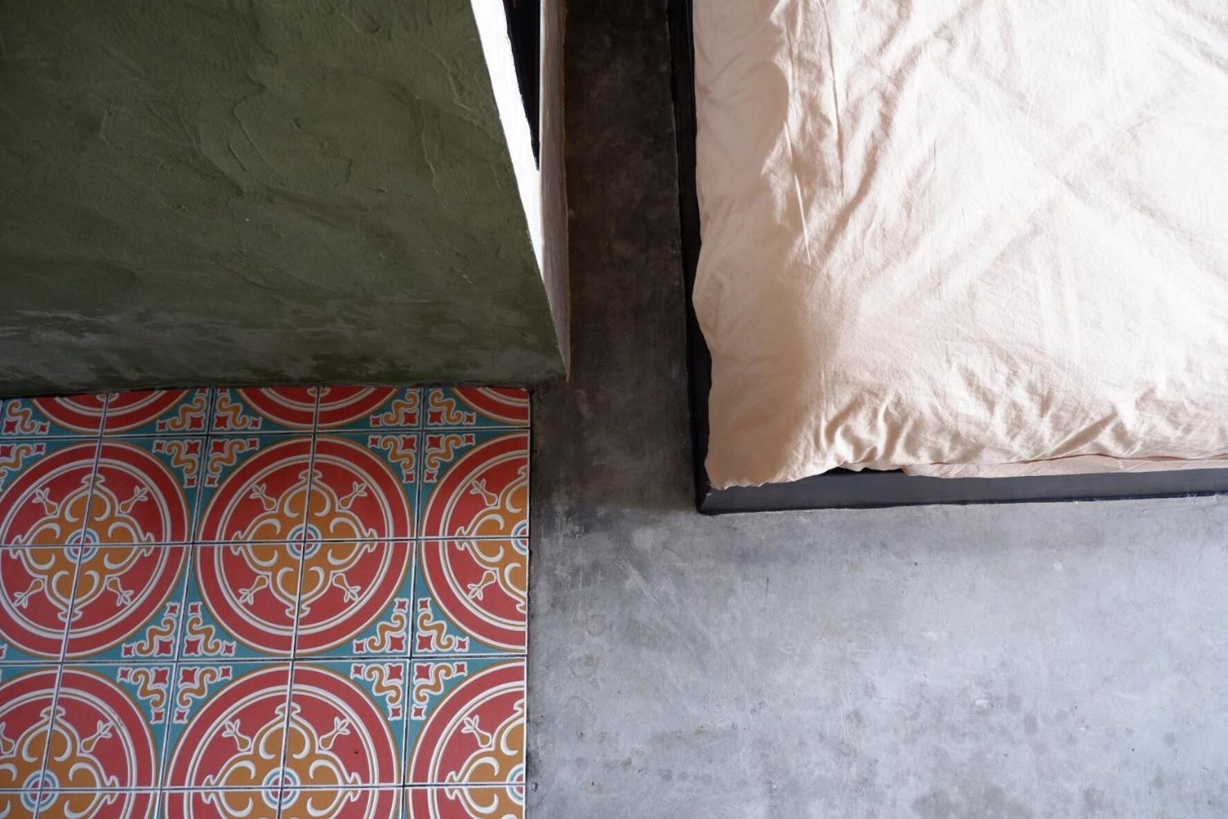 A room with a tiled floor, a green wall, and a beige mattress.