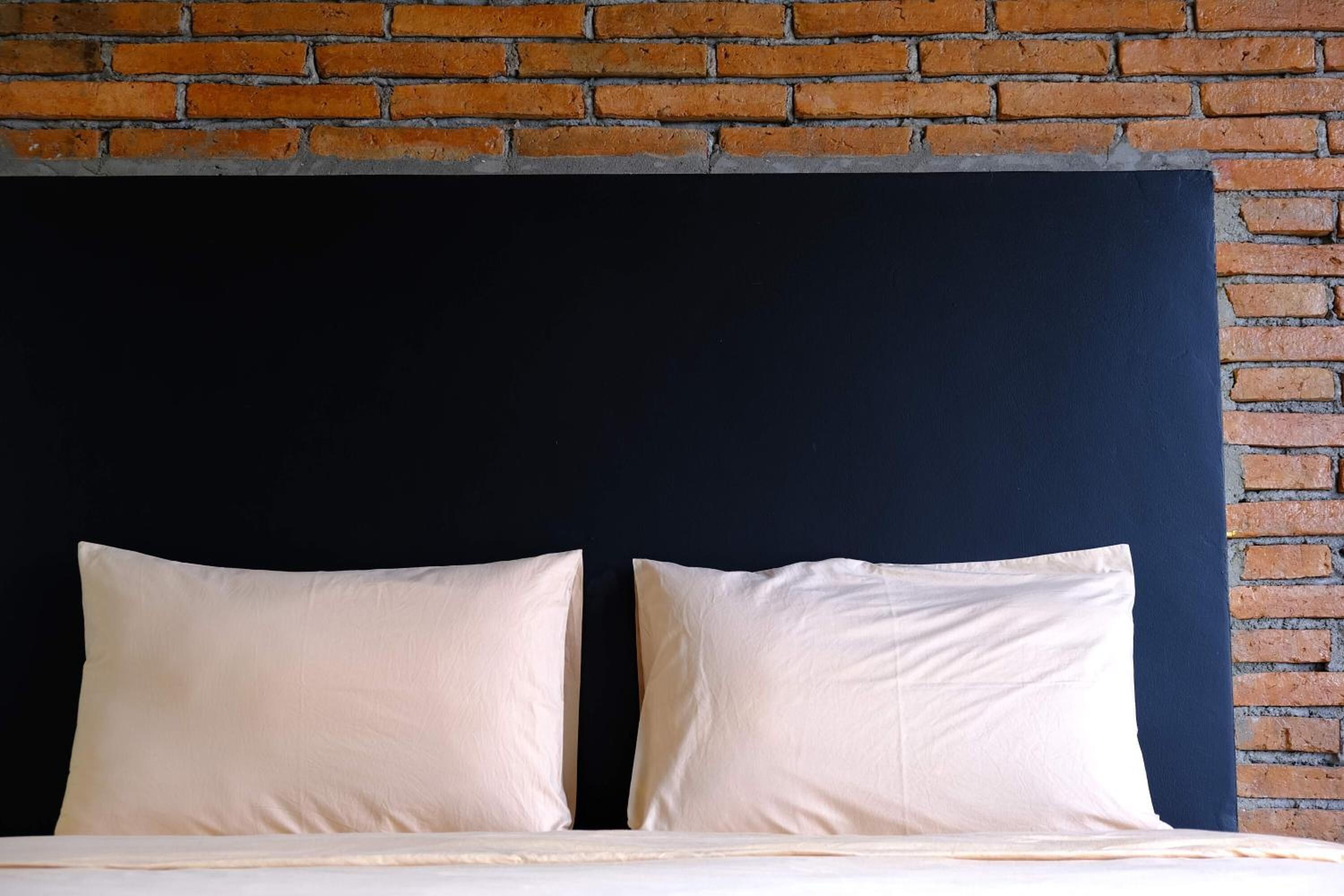 Una cama con dos almohadas frente a un muro de ladrillo.