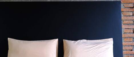 Una cama con dos almohadas frente a un muro de ladrillo.