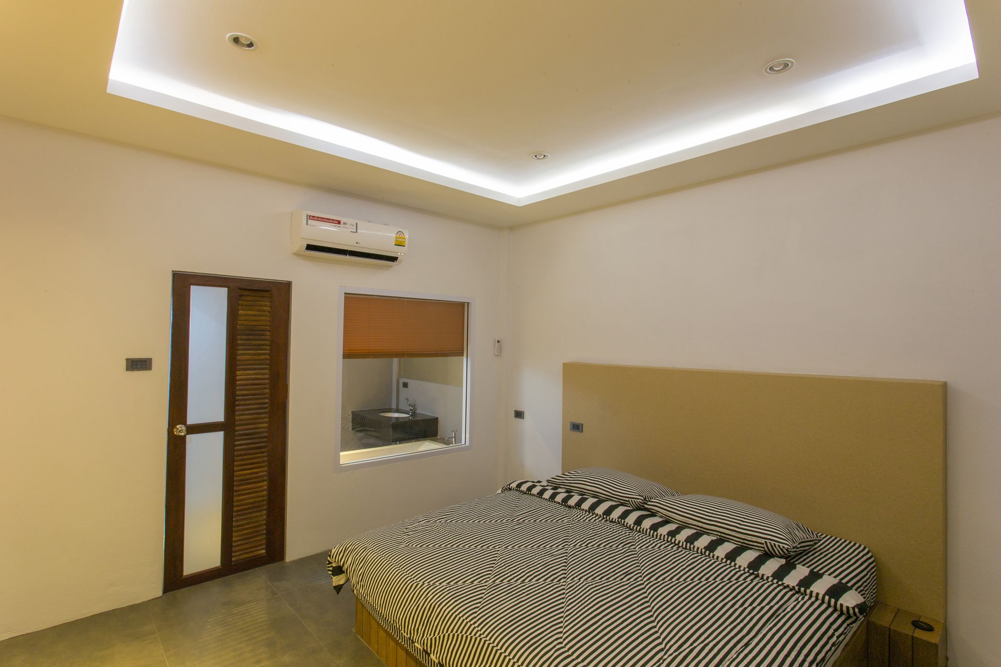 A bedroom with a skylight, a bed with striped bedding, a window with a view, and an air conditioning unit.