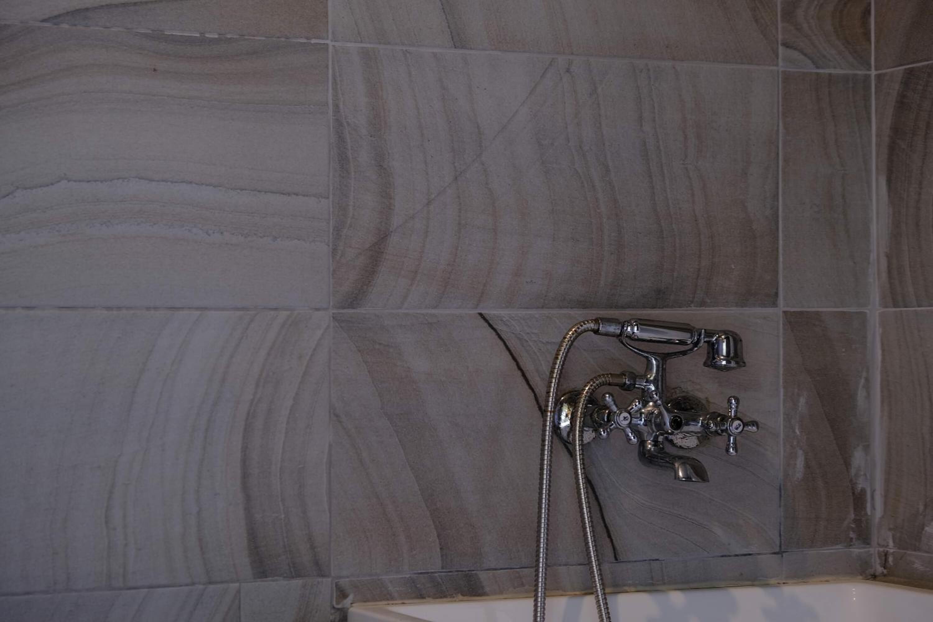 Ein Badezimmer mit einer Badewanne und einer Dusche, ausgestattet mit einem chromfarbenen Wasserhahn und Duschschlauch.