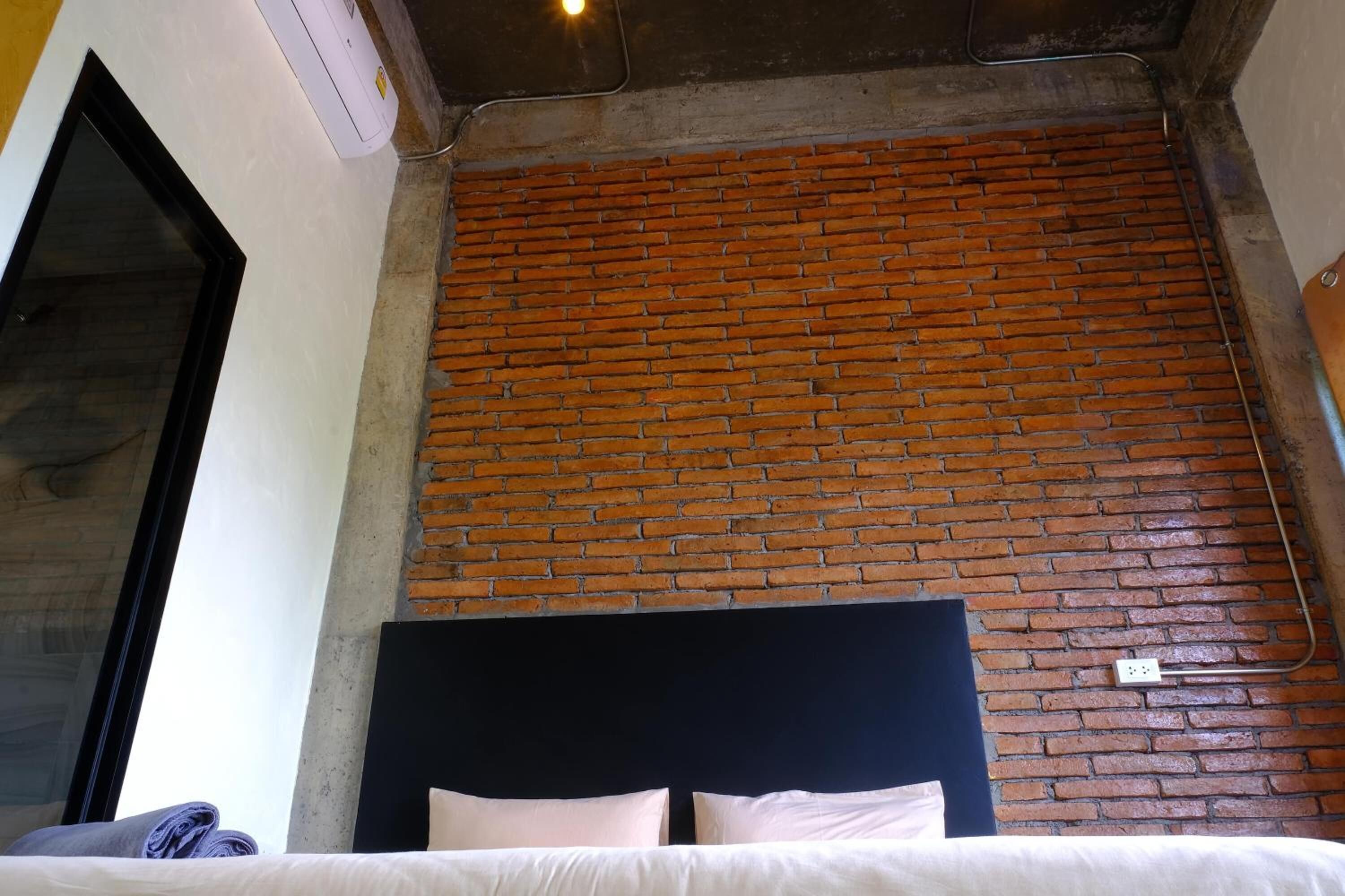 A room with a brick wall, a bed with white bedding, and a black headboard.