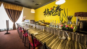 Un restaurant doté d’un long bar en bois, de chaises rouges et de murs jaunes ornés de caractères chinois.