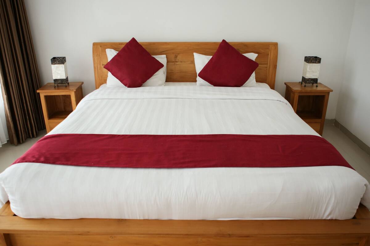 Uma cama de casal com cabeceira de madeira, duas mesas de cabeceira e um cobertor vermelho.