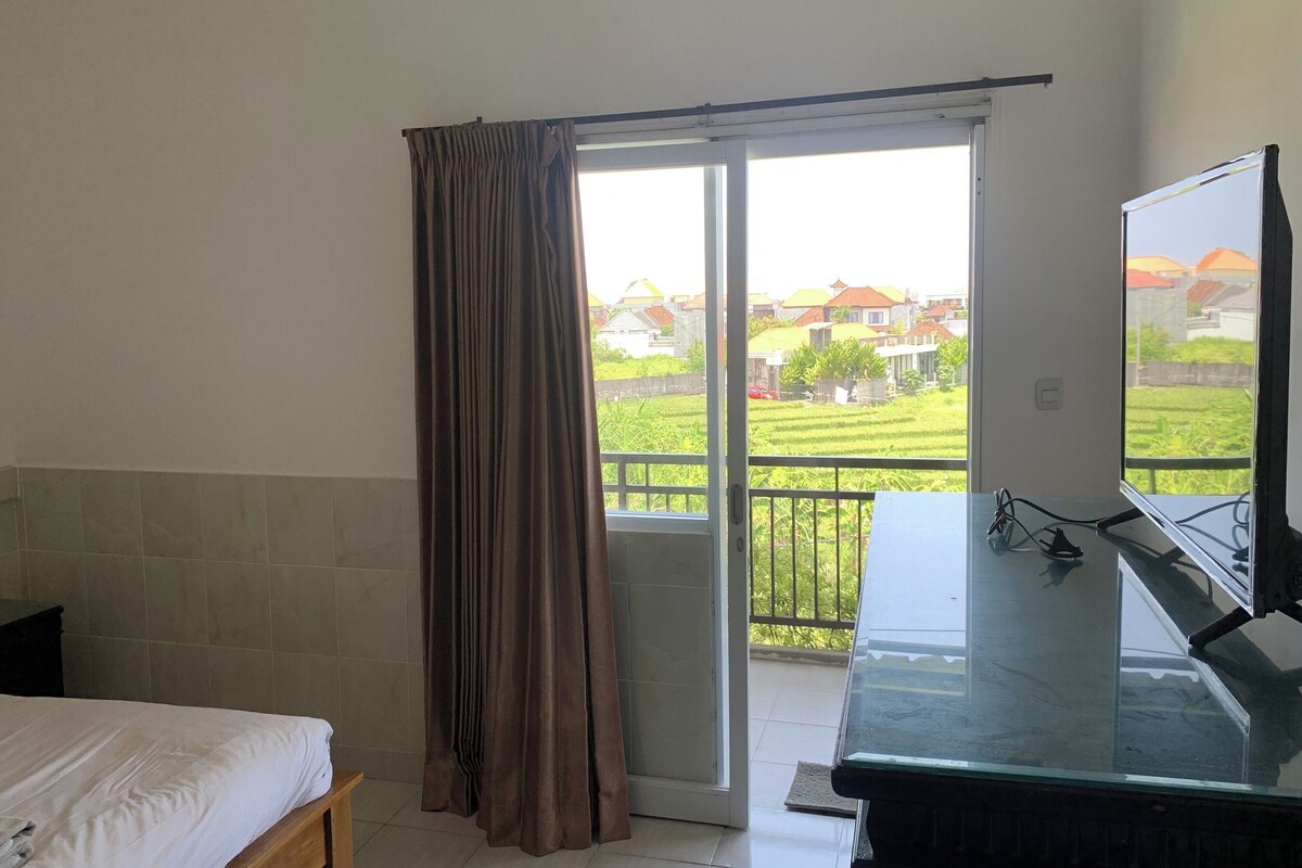 A bedroom with a bed, a sliding glass door to a balcony, and a television on a stand.
