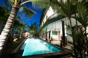 A swimming pool surrounded by palm trees and a building with a balcony. - Grandpa Guest House (Tibubeneng)