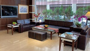 A modern living room with a large flat-screen TV, leather sofas, a glass coffee table, and a view of trees through large windows. - Young Soarlan Boutique Hotel (Tainan)