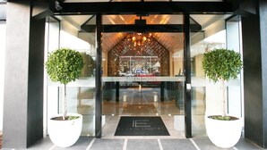Entrada d'hotel amb un disseny modern, amb façana de vidre, una entrada central i dues plantes en testos.