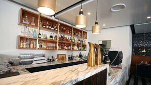 Zona de bar amb taulells de marbre, amples prestatges plens de garrafes de licors i llums penjants.