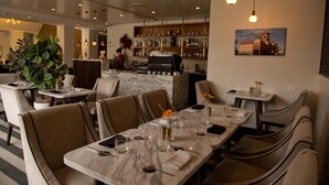 Un restaurant amb taules de marbre, caires amb coixins, una zona de bar i una gran planta en test.