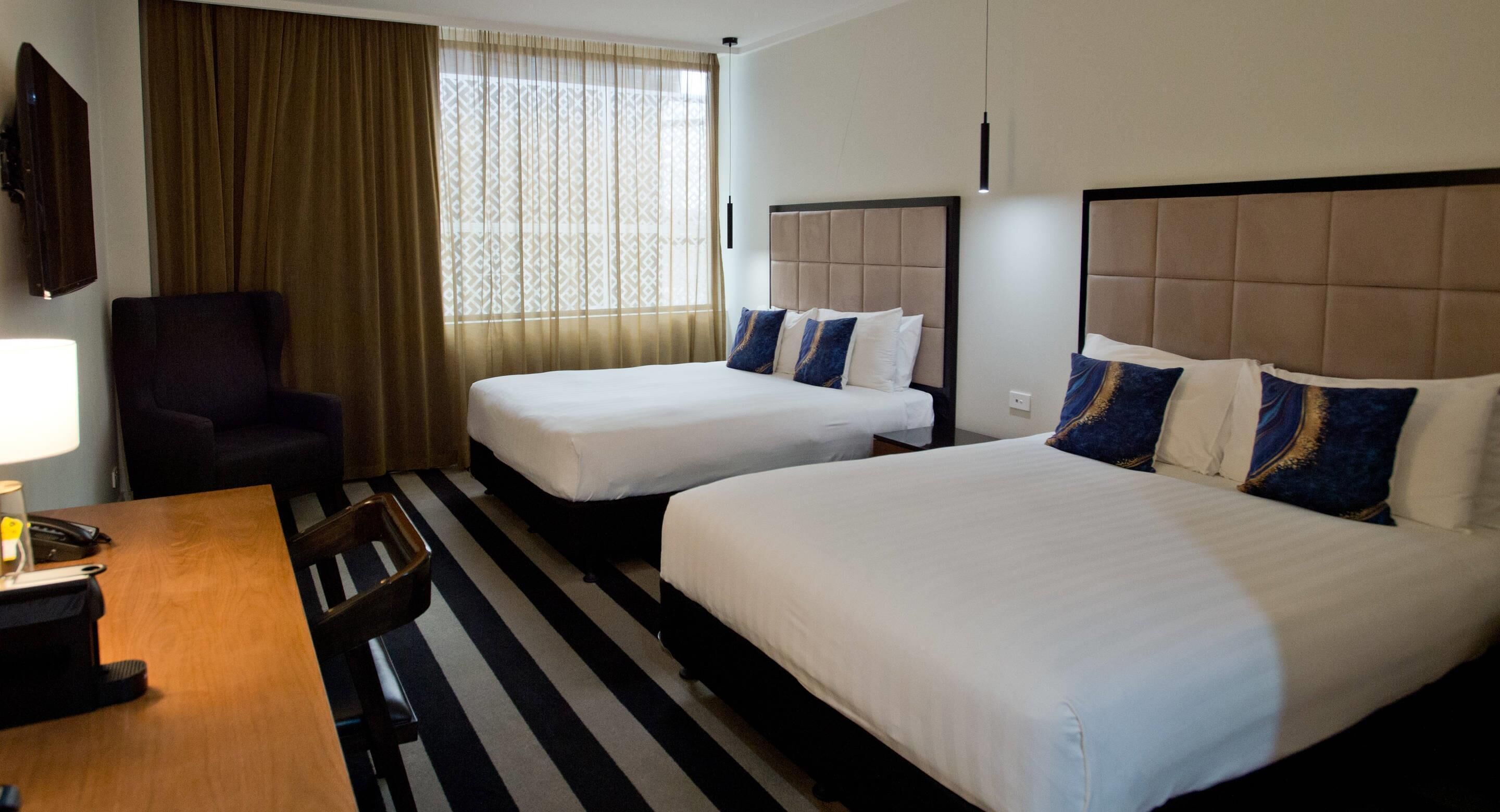 A hotel room with two beds, a desk, a chair, and a television.