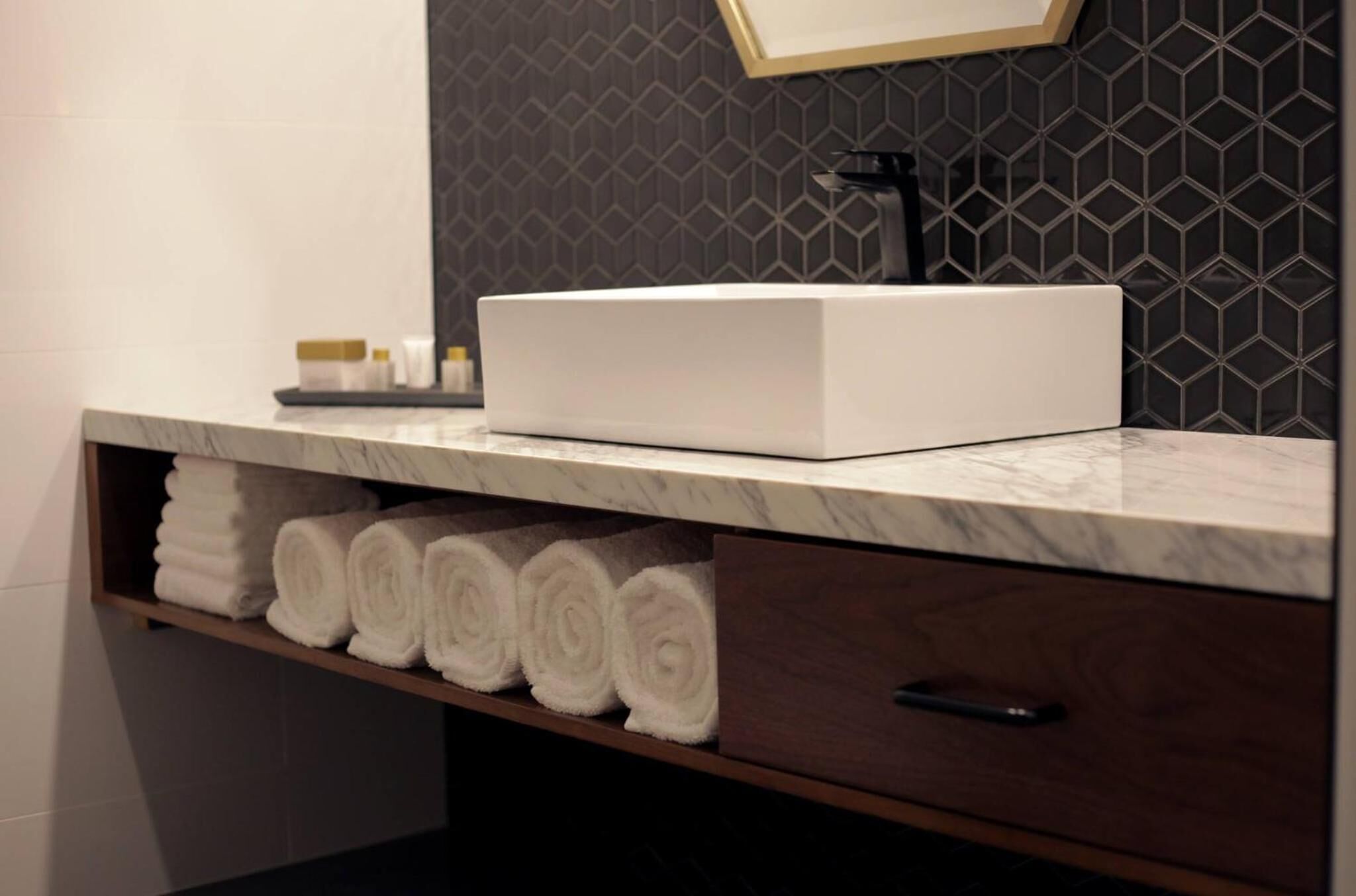 A bathroom with a white sink, a towel rack with neatly rolled towels, and a dark patterned wall.