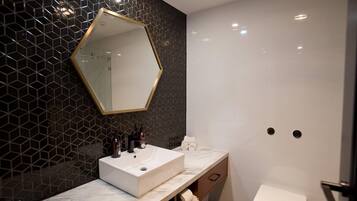 A modern bathroom with a hexagonal mirror, a white sink, and a toilet.