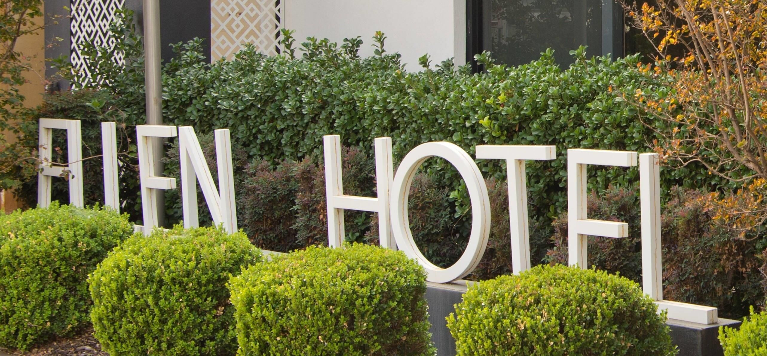 A sign with the words 'FIEN HOTEL' in large white letters, surrounded by well-maintained green hedges.